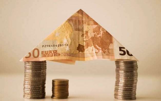 Banknote formed into a roof rests on pillars of money coins