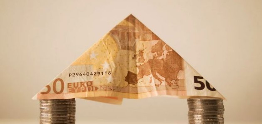 Banknote formed into a roof rests on pillars of money coins