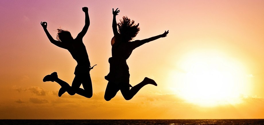2 people jumping on the beach before sunset
