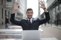 Man with arms raised in joy in front of a screen in the outdoor area of a café in a pedestrian zone