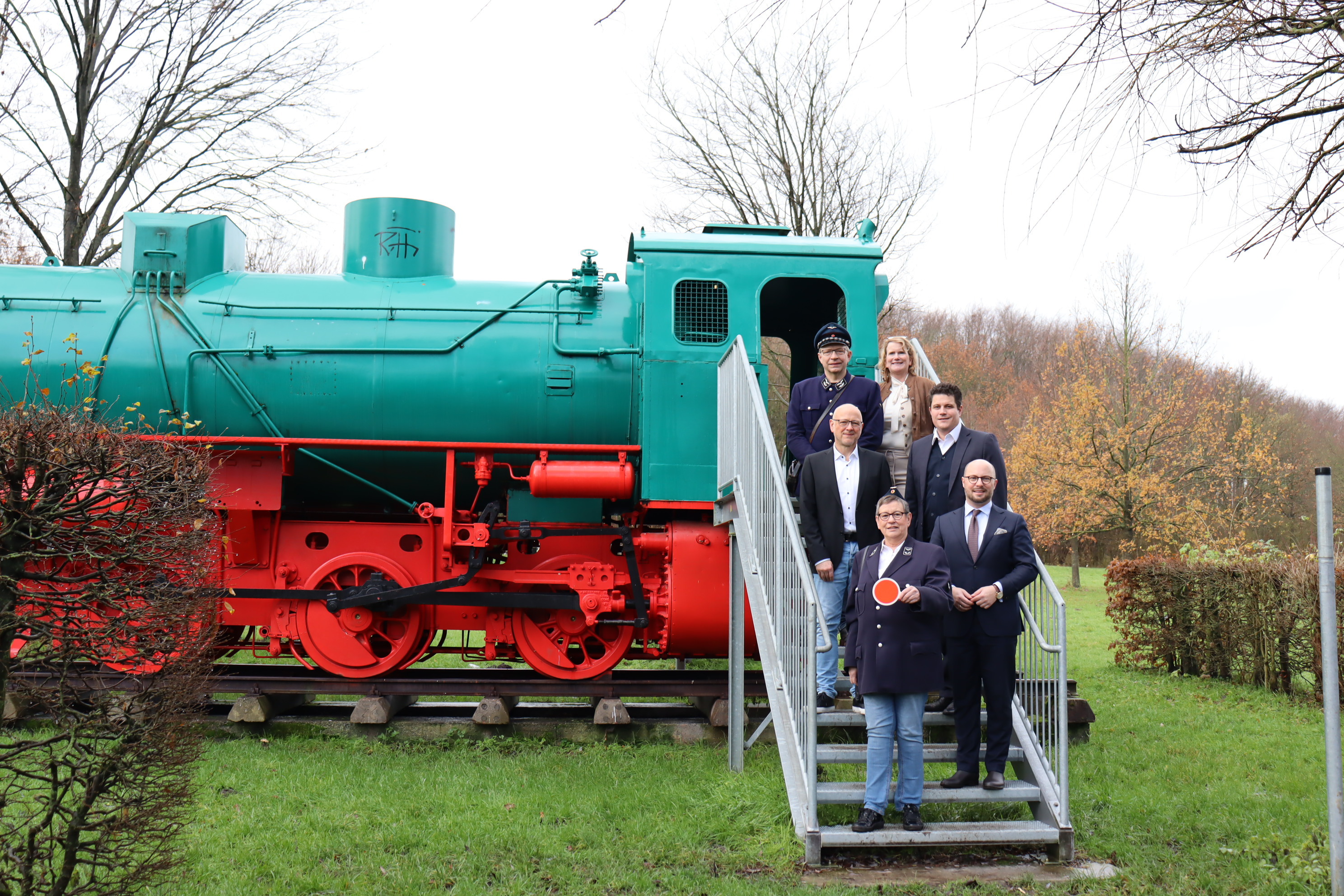 De ontmantelde locomotief in het activiteitenpark Phoenix wekt verwachtingen voor de geplande pendeldienst: onderste rij (vanaf links) Gudrun Rassat (Osnabrücker Förderkreis Eisenbahn-Tradition) en burgemeester Michael Gerdhenrich, midden: Uwe Denkert (Stad Beckum) en Dr. Daniel Dierich (Energieversorgung Beckum), bovenste rij: Burkhard Rassat (Osnabrücker Förderkreis Eisenbahn-Tradition) en Marianne Witt-Stuhr (Stad Beckum).