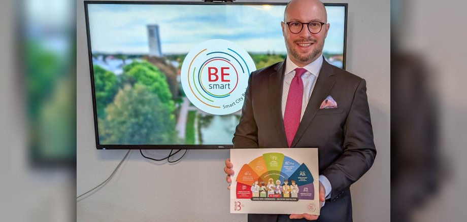 Bürgermeister Michael Gerdhenrich mit der Broschüre vor dem Video