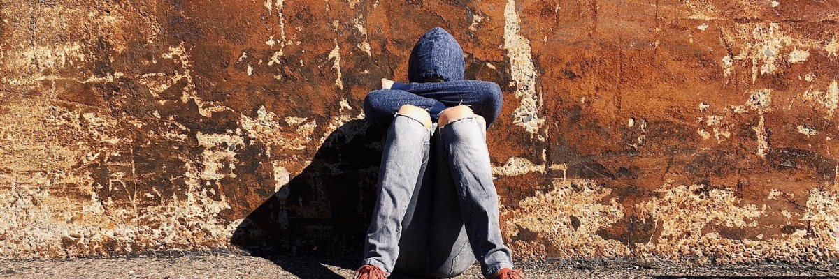 An einer Hauswand kniender Jugendlicher, der sein Gesicht in den Knien vergräbt