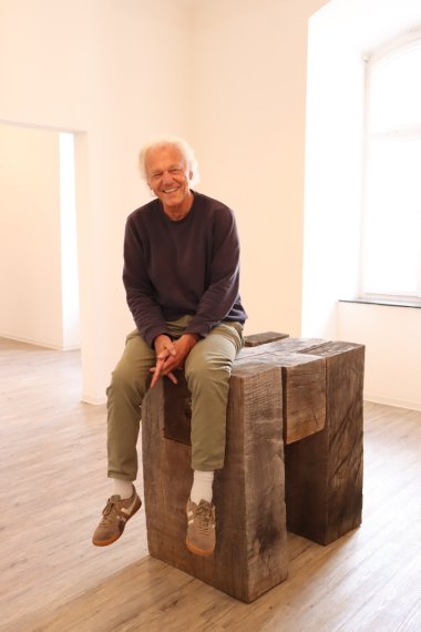 Künstler sitzt auf Kunstwerk aus Holz