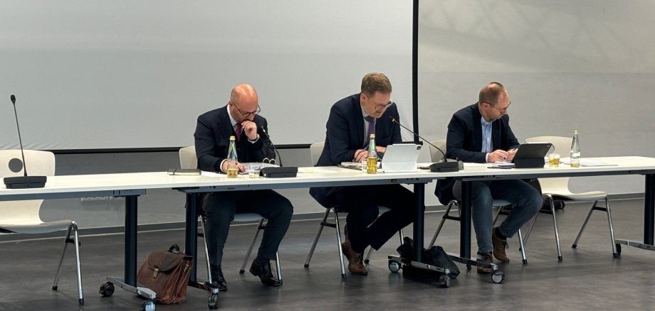 Wahlleiter mit Bürgermeister und Ratsbüro-Mitarbeitendem in der Ratssitzung